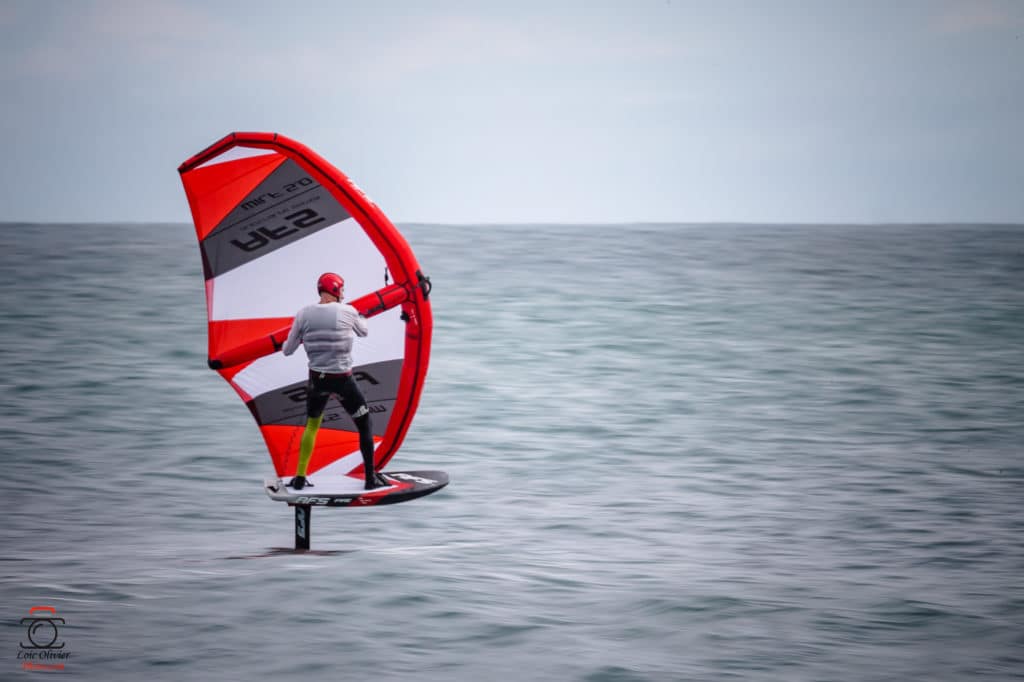 Un homme faisant de la planche à voile dans l'océan avec une voile rouge et blanche
