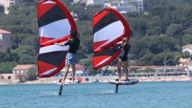 Deux personnes font de la planche à voile sur l'eau avec des voiles rouges et noires